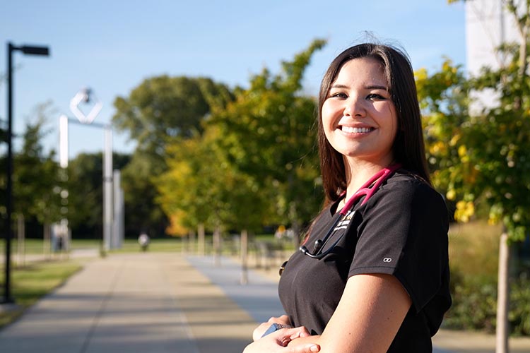 A Purdue University Northwest nursing student poses outdoors, in front of the Bell Tower