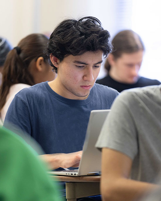 A student in a blue shirt types on a laptop