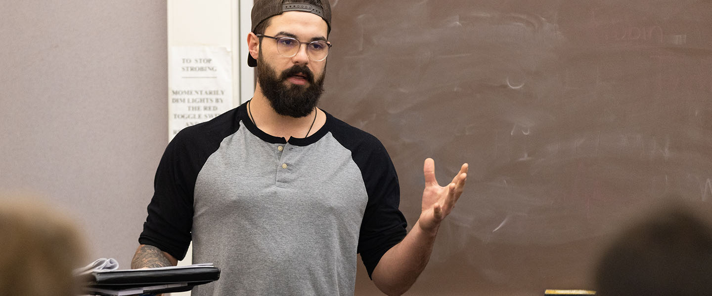 A PNW student stands in front of a classroom.