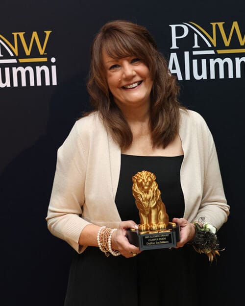 Debbie Bachman poses in front of a PNW Alumni backdrop with her Alumni Award.