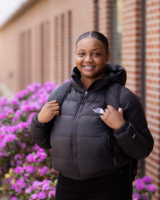 A PNW student in a winter coat poses in front of flowers