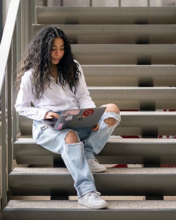 A PNW student works on a laptop on a stairway