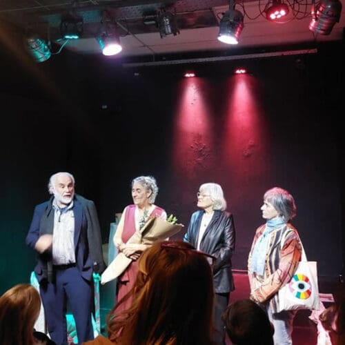 Jose Castro Urioste, Nora Ugartemendia, Maria Ines Martinez, and Graciela Balletti stand on stage in a spotlight.