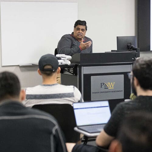 A PNW professor sits at a podium during a class.