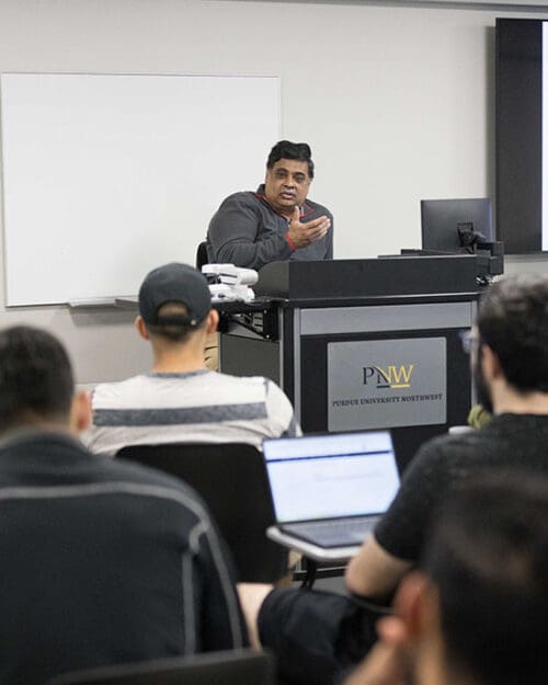 A PNW professor sits at a podium during a class.