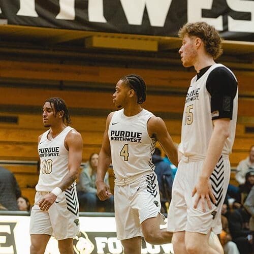 Three men's basketball players with white jerseys on in the PNW gym