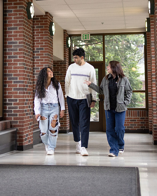 Three PNW students walk through a hallway that is lined with windows.