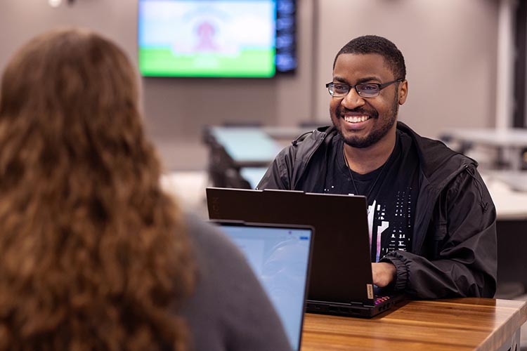 A PNW student with a laptop collaborates with a friend on campus.