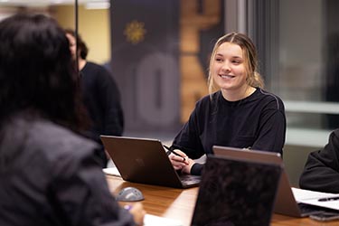 A PNW student collaborates with friends on laptops at a conference table.