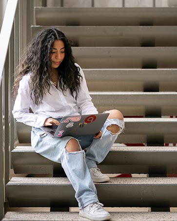 A PNW student works on a laptop on a stairway.