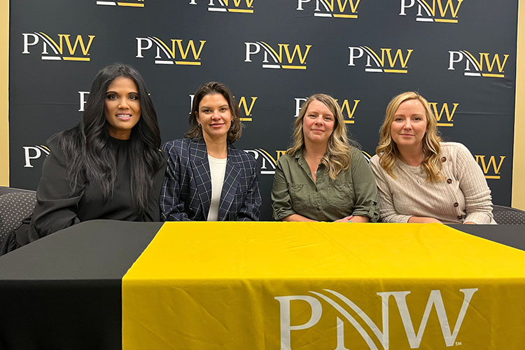 Nicky Ali Jackson, Maureen Bauer, Nicole Schmidt and Tara Petito sit together at a table. There is a step and repeat featuring the PNW logo behind them.