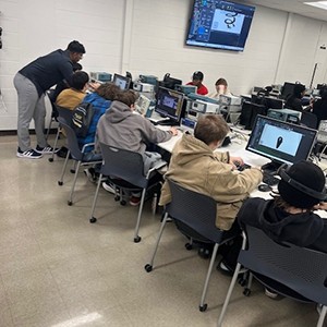 Students sit at a line of computers.
