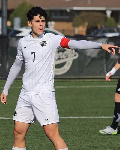 A PNW player in white number 7 soccer uniform and red armband points on the field