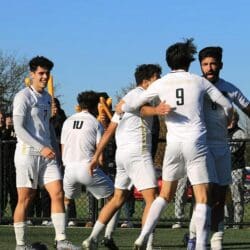 Soccer players in white uniforms celebrate together outdoors