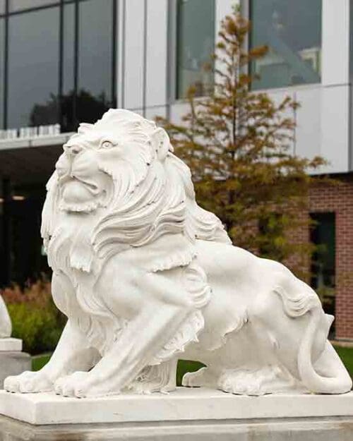 A white lion statue on the PNW Hammond Campus. There is a tree and the Nils Bioscience building in the background.