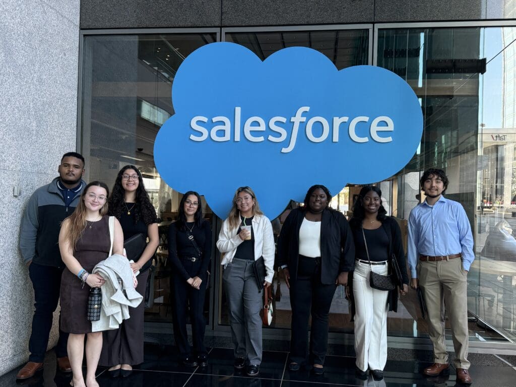 Diverse group of eight students in front of Salesforce sign