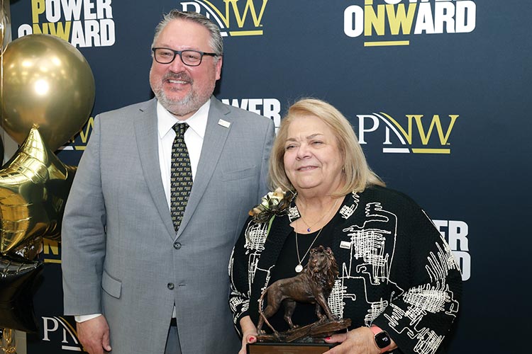 PNW Chancellor Chris Holford and PNW Alumni Hall of Fame Inductee Diane Kavadias Schneider at the 2024 Hall of Fame induction ceremony. Schneider is holding a lion statuette.