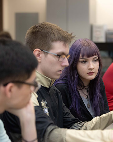 Three students sit in a classroom, they are all looking at a computer screen.