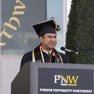 PNW alumni and student graduation speaker Felipe Oria stands at a podium during a commencement ceremony