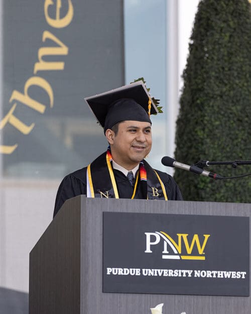 PNW alumni and student graduation speaker Felipe Oria stands at a podium during a commencement ceremony