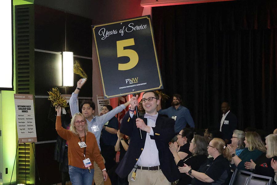 A man holding a 5 Years of Service slide leads a procession.