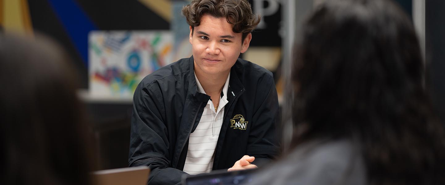 Male student talking with a group of people on campus 1440x600