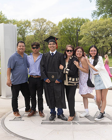 A student poses with their family under the PNW Bell Tower during commencement.