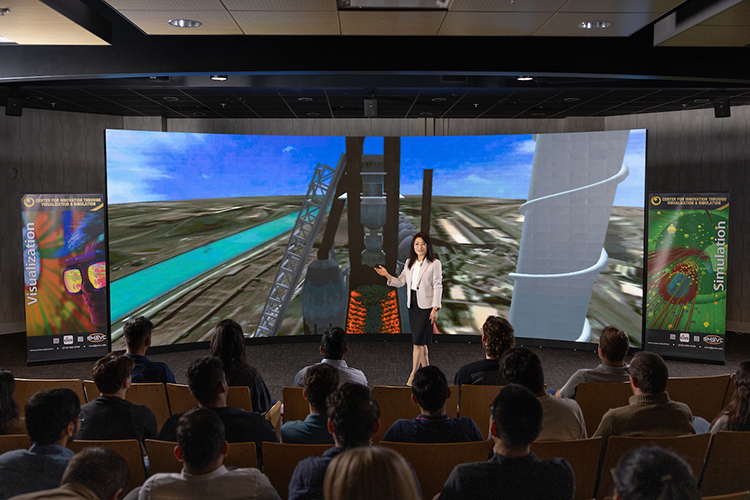 Chenn Zhou stands on stage in front of a blast furnace visualization.
