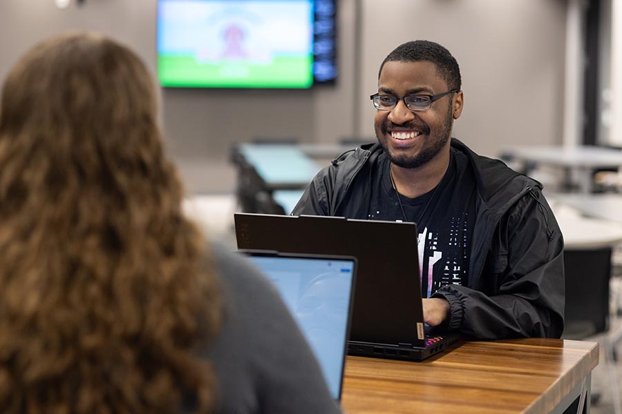 Two PNW students talking to each other while on their computers