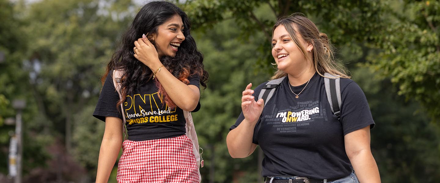Two PNW students walking and laughing outside on campus in PNW t-shirts 1440x600