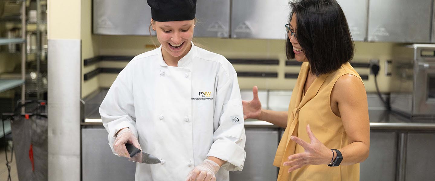PNW student in HTM and professor talking to one another while student slices vegetables 1440x600