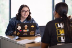 A PNW student works behind a laptop covered in stickers.