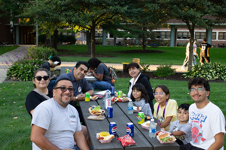 A family sits at a picnic table and eats lunch.