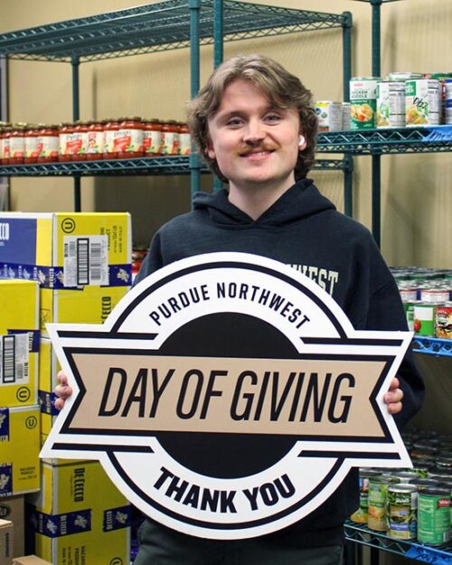 A student in the PNW Food Pantry holds a Purdue Northwest Day of Giving "Thank You" sign.
