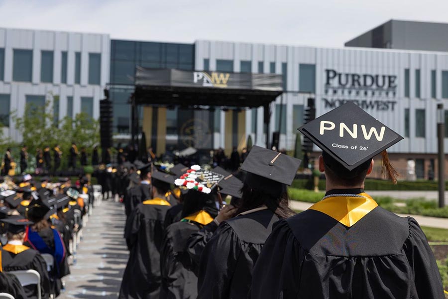 Purdue Northwest graduates line up for Commencement. One wears a Class of 2026 PNW cap.