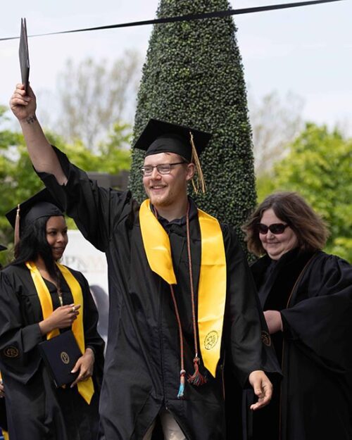 A student walks across the stage and holds up their diploma cover.