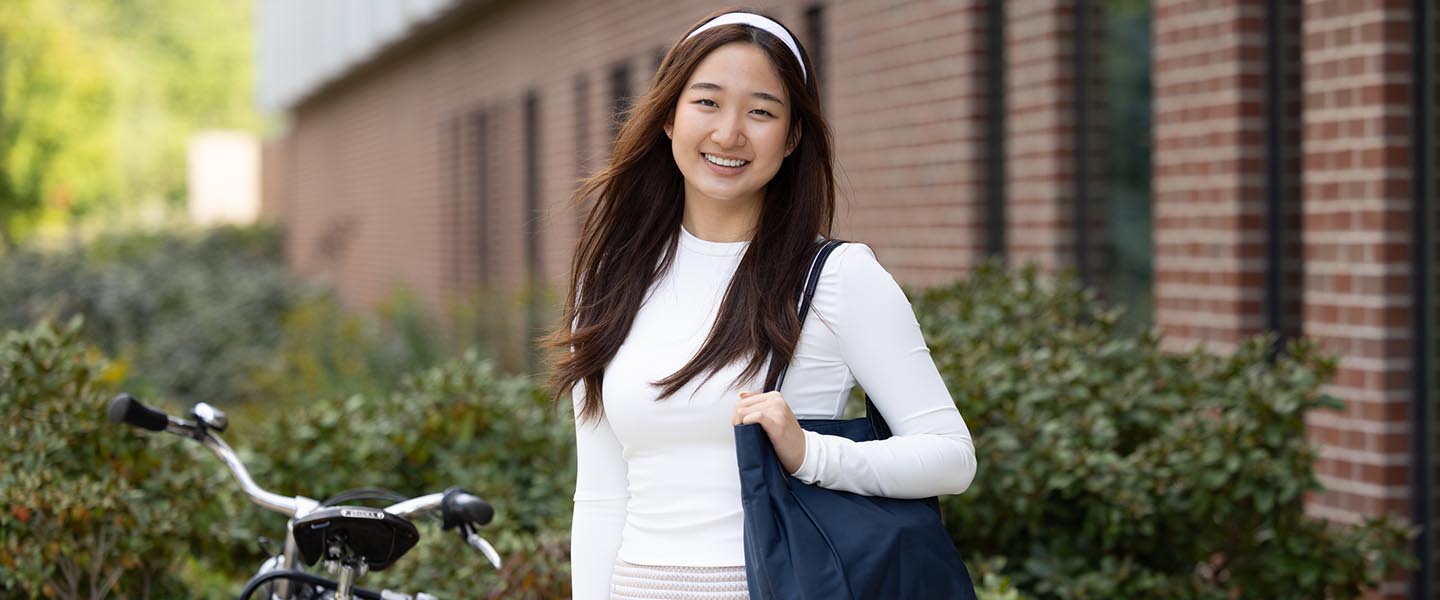 PNW student posing outside on campus while holding a bag 1440x600
