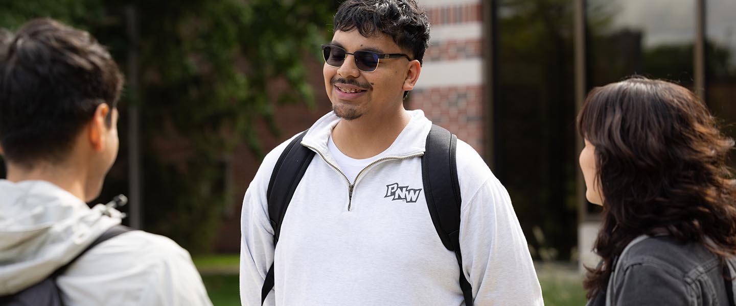 Three PNW students talking outside on campus 1440x600