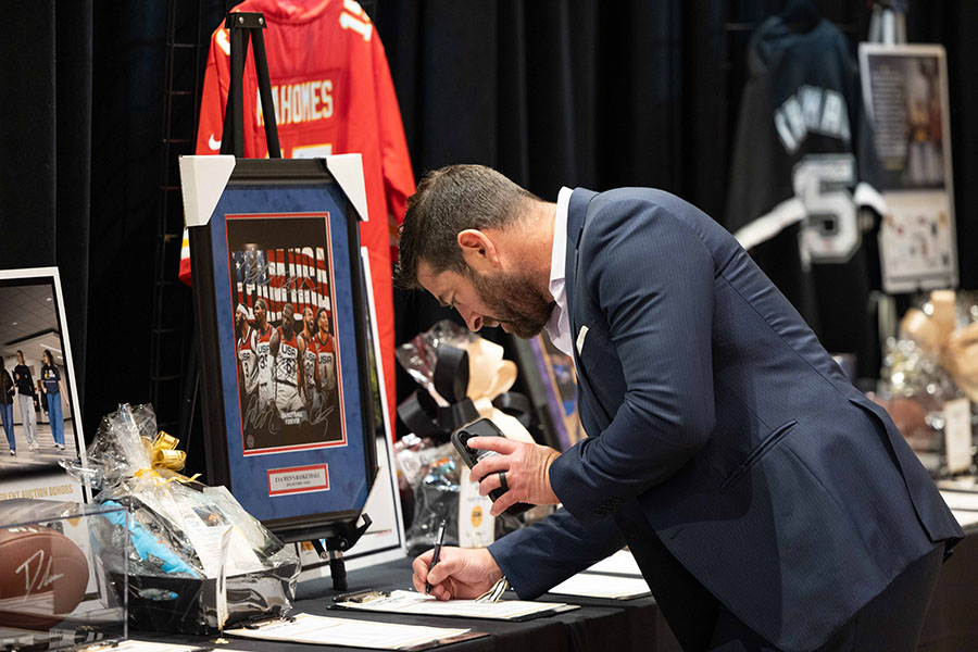 A person stands at a silent auction table and adds a bid.