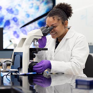 A PNW student in a lab coat looks through a microscope