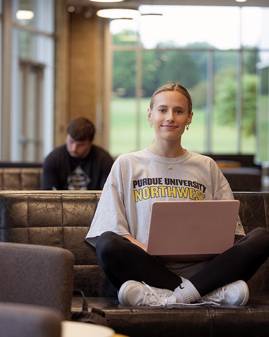 A PNW student works on a laptop in a campus lounge.