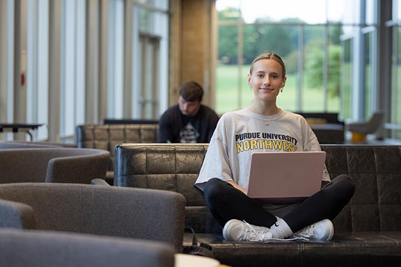 A PNW students works on her laptop in a campus lounge.