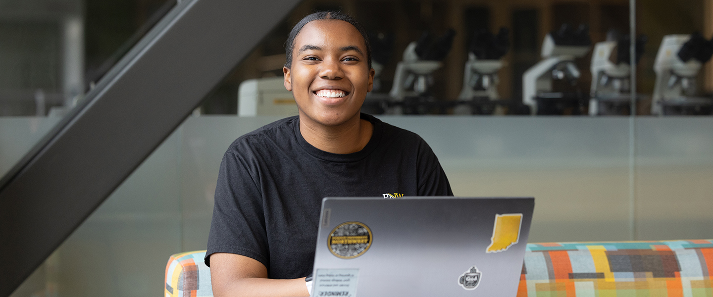 A student sits at a desk space with a laptop open in front of them.