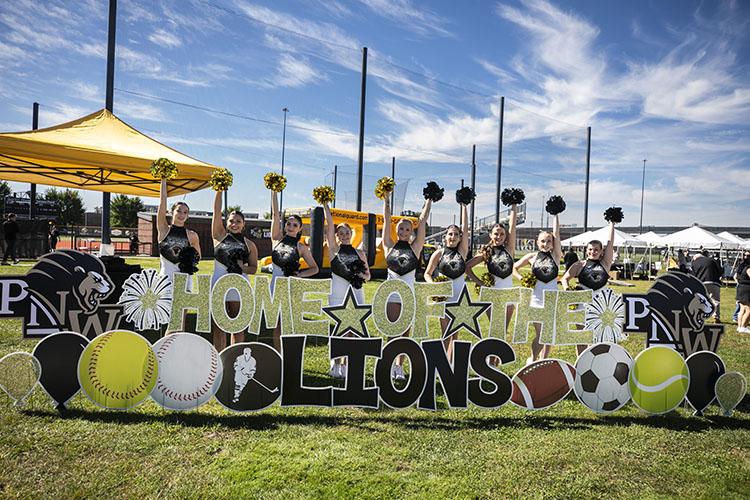 PNW dance team members stand in front of a yard sign that reads: Home of the Lions.