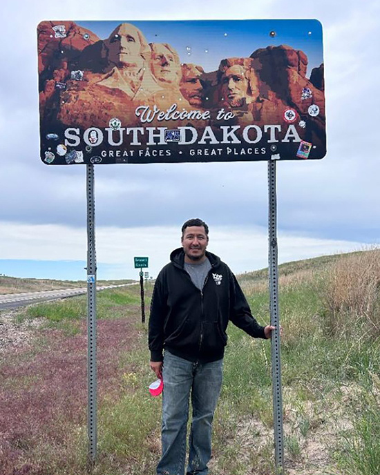 Hugo Garcia standing under a sign that reads: Welcome to South Dakota