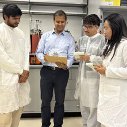 Three students stand with Professor Veera Gnaneswar Gude in a lab space.