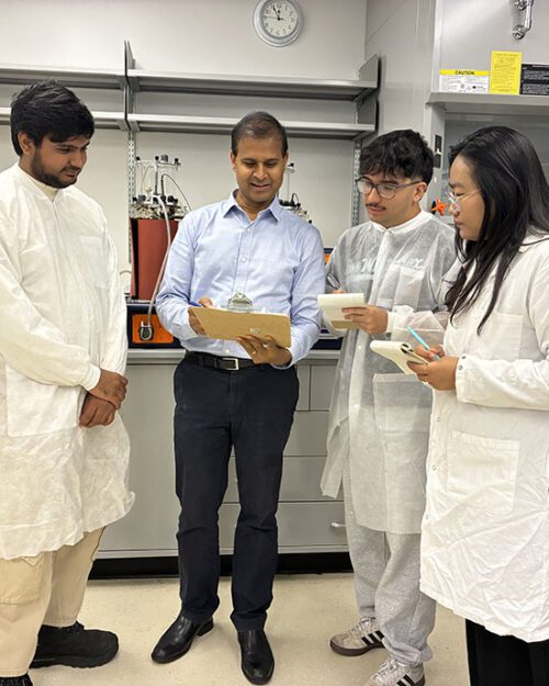 Three students stand with Professor Veera Gnaneswar Gude in a lab space.