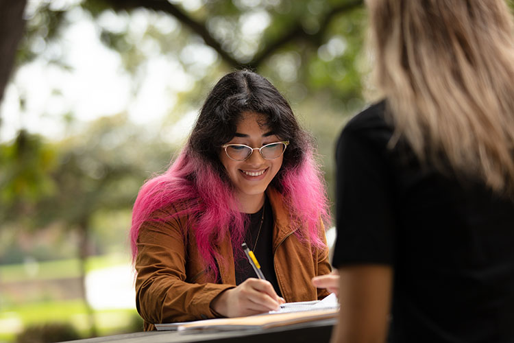 A student sits outside and writes in a notebook