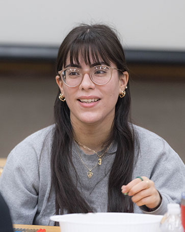 A student sits at a desk. They are looking off camera and talking