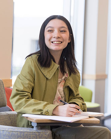 A student sits at a desk and smiles